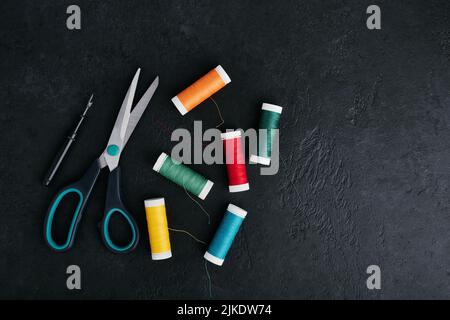 Reels of thread scattered on the table, tailors scissors and thread cutter, dark background Stock Photo