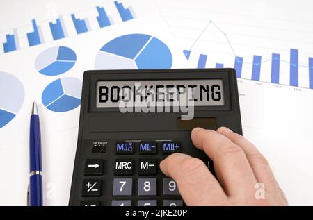 Business concept. There is a calculator on documents with graphs and diagrams. On the scoreboard of the calculator is the inscription - Bookkeeping Stock Photo