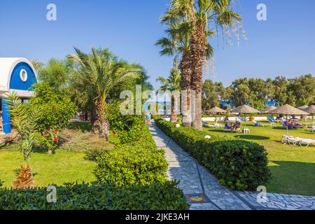 Beautiful view of green outdoor pool area and pathway to beach on blue sea water and cloudless sky background. Rhodes. Greece. Stock Photo