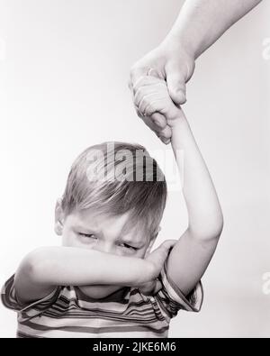 1960s CRYING LITTLE BOY COVERING HIS FACE WITH ONE ARM THE OTHER RAISED HOLDING AS MAN’S HAND FATHER OR TEACHER - j11770 DEB001 HARS RAISED TIRED LIFESTYLE EXHAUSTED STUDIO SHOT MOODY TEARS HOME LIFE COPY SPACE CRY MALES AFRAID COVERING TROUBLED B&W CONCERNED SADNESS EYE CONTACT WEEPING HEAD AND SHOULDERS DISCOVERY HIS PROTECTION BRAT LOW ANGLE BAWLING HURT MOOD SOBBING CONCEPTUAL GLUM ESCAPE SPOILED SUPPORT DEB001 MAN'S ACTING OUT OR BEHAVIOR JUVENILES MISERABLE BLACK AND WHITE CAUCASIAN ETHNICITY HANDS ONLY OLD FASHIONED Stock Photo