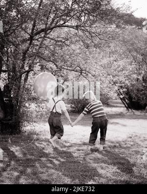 1960s LITTLE BOY AND GIRL HOLDING HANDS WALKING IN GRASS GIRL BAREFOOT HOLDING A BALLOON BOTH WEARING BLUE JEANS TEE SHIRTS - j13216 HAR001 HARS JOY LIFESTYLE FEMALES BROTHERS NATURE TEE COPY SPACE FRIENDSHIP FULL-LENGTH PERSONS MALES SIBLINGS DENIM SISTERS B&W SUMMERTIME HIGH ANGLE ADVENTURE AND SHIRTS BAREFOOT SIBLING CONNECTION FRIENDLY BLUE JEANS COOPERATION GROWTH INFORMAL JUVENILES SEASON TOGETHERNESS TWILL BLACK AND WHITE CASUAL CAUCASIAN ETHNICITY HAR001 OLD FASHIONED Stock Photo