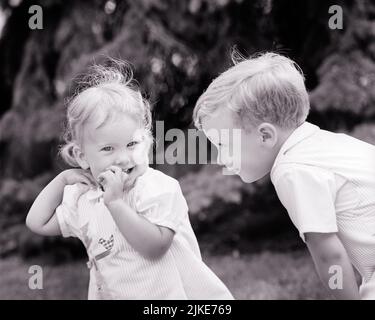 1970s BABY GIRL TODDLER SMILING LOOKING AT CAMERA UNDER THE WATCHFUL EYE OF HER OLDER BROTHER - j13469 HAR001 HARS PLEASED FAMILIES JOY LIFESTYLE FEMALES WINNING BROTHERS HEALTHINESS HOME LIFE COPY SPACE FRIENDSHIP HALF-LENGTH PERSONS CARING MALES SIBLINGS SISTERS B&W HAPPINESS CHEERFUL PROTECTION SIBLING SMILES CONNECTION JOYFUL PERSONAL ATTACHMENT PLEASANT AFFECTION AGREEABLE CHARMING COOPERATION EMOTION GROWTH JUVENILES LOVABLE PLEASING TOGETHERNESS ADORABLE APPEALING BABY GIRL BLACK AND WHITE CAUCASIAN ETHNICITY HAR001 OLD FASHIONED WATCHFUL Stock Photo