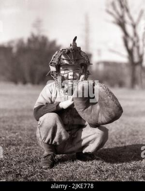 1930s LITTLE BOY WEARING BASEBALL UNIFORM IN TRADITIONAL CATCHER’S STANCE WEARING FACE MASK GUARD AND CATCHER’S MITT  - j1324 HAR001 HARS INSPIRATION TRADITIONAL MALES RISK CONFIDENCE B&W CATCHING HAPPINESS CHEERFUL LITTLE LEAGUE ADVENTURE LEISURE PROTECTION STRATEGY CATCHER MITT SQUAT AND EXCITEMENT LOW ANGLE RECREATION SMILES CONCEPTUAL JOYFUL SUPPORT BALL GAME BALL SPORT COOPERATION GROWTH JUVENILES POSITION BASEBALL BAT BLACK AND WHITE CAUCASIAN ETHNICITY HAR001 OLD FASHIONED SQUATTING STANCE Stock Photo