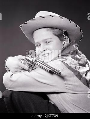 1950s SMILING BOY IN COWBOY COSTUME HAT NECKERCHIEF HOLDING A TOY PISTOL LOOKING AT CAMERA - j3282 HAR001 HARS WESTERN CONFIDENCE B&W EYE CONTACT COWBOYS DREAMS HUMOROUS HAPPINESS HEAD AND SHOULDERS CHEERFUL ADVENTURE COMICAL PRIDE NECKERCHIEF SMILES CONCEPTUAL COMEDY IMAGINATION JOYFUL CAP PISTOL SIX GUN FIREARM FIREARMS JUVENILES PISTOL SIX SHOOTER BLACK AND WHITE CAUCASIAN ETHNICITY HAR001 OLD FASHIONED Stock Photo