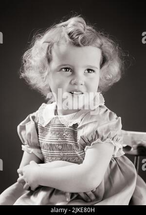 1940s BLONDE GIRL ARMS CROSSED CURLY HAIR WEARING DRESS WITH STITCHED SMOKING LOOKING OFF CAMERA - j387 HAR001 HARS JOY LIFESTYLE FEMALES HALF-LENGTH EXPRESSIONS B&W CHEERFUL CURLY SMILES CONCEPTUAL JOYFUL PLEASANT JUVENILES STITCHED BABY GIRL BLACK AND WHITE CAUCASIAN ETHNICITY HAR001 OLD FASHIONED Stock Photo