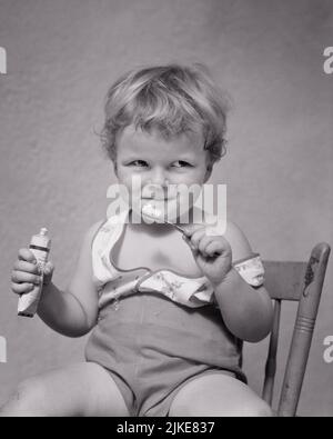 1930s CUTE BLONDE TODDLER BOY SMILING HOLDING TOOTHBRUSH AND TUBE OF TOOTHPASTE LOOKING OFF CAMERA WITH IMPISH GRIN - j4336 HAR001 HARS MALES B&W EYE CONTACT GOALS TEMPTATION HUMOROUS CHEERFUL AND PLAYFUL SLY COMICAL HANDSOME MISCHIEVOUS OPPORTUNITY SMILES CONCEPTUAL COMEDY JOYFUL BABY BOY IMPISH PLEASANT AGREEABLE CHARMING COOPERATION GRIN GROWTH JUVENILES LOVABLE PLEASING ADORABLE APPEALING BLACK AND WHITE CAUCASIAN ETHNICITY HAR001 OLD FASHIONED