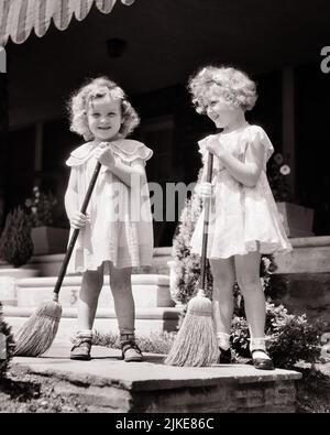 1930s TWO SMILING CURLY HAIRED GIRLS IN CUTE SUMMER DRESSES HOLDING BROOMS SWEEPING THE SIDEWALK IN FRONT OF THE HOUSE PORCH - j5366 HAR001 HARS FRIEND TEAMWORK TWIN IDENTICAL DOUBLE PLEASED JOY LIFESTYLE SATISFACTION FEMALES HOUSES HEALTHINESS HOME LIFE COPY SPACE FRIENDSHIP FULL-LENGTH BROOM RESIDENTIAL MATCH BUILDINGS SIBLINGS SISTERS B&W SUMMERTIME EYE CONTACT DRESSES GOALS MATCHING SAME HAPPINESS CHEERFUL SWEEPING LOW ANGLE CURLY MARY JANE PRIDE BROOMS HAIRED HOMES SIBLING SMILES FRIENDLY JOYFUL RESIDENCE STYLISH SUPPORT IN FRONT OF LOOK-ALIKE COOPERATION DUPLICATE GROWTH JUVENILES Stock Photo