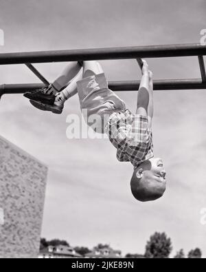 1950s BOY HANGING UPSIDE DOWN ON PLAYGROUND MONKEY BARS  - j5851 HAR001 HARS JUNGLE HEALTHINESS ATHLETICS HORIZONTAL COPY SPACE FULL-LENGTH DANGER MALES RISK ATHLETIC UPSIDE B&W BARS ACTIVITY HUMOROUS HAPPINESS PHYSICAL ADVENTURE STRENGTH STUNT CHALLENGE EXCITEMENT LOW ANGLE RECREATION ATHLETES FLEXIBILITY MUSCLES GROWTH JUVENILES BLACK AND WHITE BRAVE CAUCASIAN ETHNICITY DARING HAR001 MONKEY BARS OLD FASHIONED UPSIDE DOWN Stock Photo