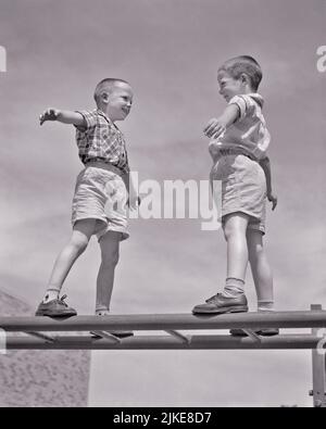 1950s TWO SMILING BOYS FACING EACH OTHER ARMS OUT FOR BALANCE STANDING ON TOP OF MONKEY BARS PLAYGROUND SET  - j7510 HAR001 HARS FITNESS SHORTS JUVENILE YARD ELEMENTARY STYLE HEALTHY FRIEND BALANCE COMPETITION ATHLETE PLEASED JOY LIFESTYLE JUNGLE SATISFACTION BROTHERS HEALTHINESS HOME LIFE ATHLETICS FACING HORIZONTAL COPY SPACE FRIENDSHIP FULL-LENGTH PHYSICAL FITNESS DANGER MALES RISK ATHLETIC SIBLINGS BALANCING B&W SUMMERTIME SCHOOLS ACTIVITY GRADE HAPPINESS PHYSICAL CHEERFUL ADVENTURE STRENGTH CONTEST EXCITEMENT LOW ANGLE PRIDE PRIMARY SIBLING SMILES FACE TO FACE ATHLETES FLEXIBILITY Stock Photo