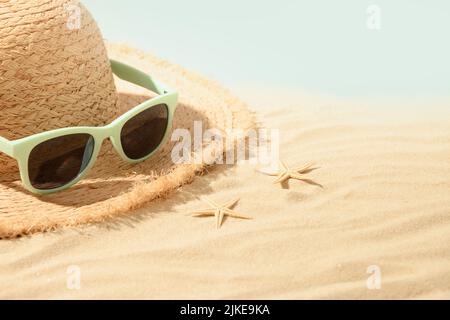 Beach straw sun hat, seashells and eyeglasses on sand. Summer holiday vacation. Stock Photo