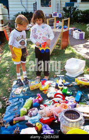 1990s YOUNG GIRL SHOWING LITTLE BOY A FRIEND TOYS SHE IS SELLING AT PARENTS SUBURBAN HOUSE FRONT YARD FLEA MARKET GARAGE SALE  - kj13321 NET002 HARS COMMUNICATION FRIEND INFORMATION JOY LIFESTYLE FEMALES HOUSES BROTHERS SHOWING RURAL HOME LIFE COPY SPACE FRIENDSHIP FULL-LENGTH PERSONS RESIDENTIAL MALES BUILDINGS SIBLINGS SISTERS GOALS IS SELLING HIGH ANGLE ADVENTURE VICTORY NETWORKING EXCITEMENT EXTERIOR SHE A AT HOMES SIBLING FRIENDLY RESIDENCE FLEA COOPERATION GROWTH SHOWS CAUCASIAN ETHNICITY OLD FASHIONED Stock Photo