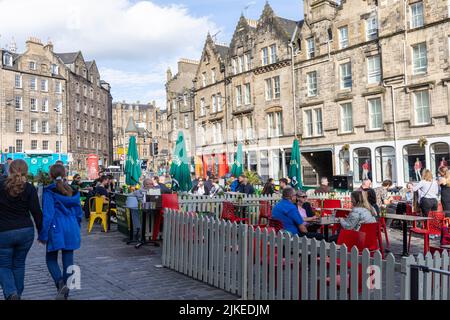 Edinburgh Grassmarket summers day 2022, people at bars and restaurants sit outside enjoying drinks and food in the sunshine,UK,2022