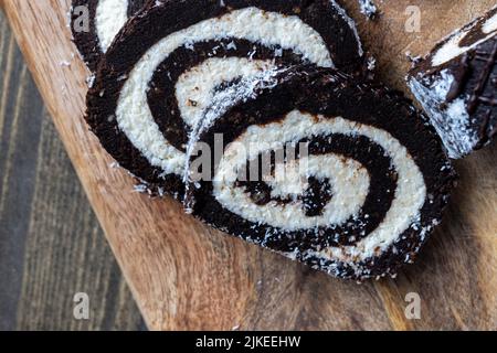 chocolate roll with a creamy curd layer in coconut chips, a roll of cakes and cottage cheese cut into pieces Stock Photo