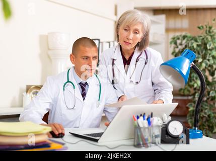 Two physicians working with case histories on laptop in office Stock Photo