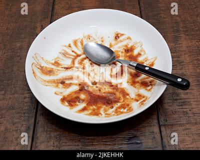 Empty dirty white bowl and spoon on a wooden table after a meal of chili or thick soup. Stock Photo