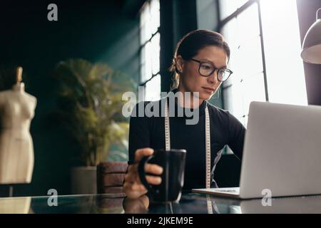 Female dress designer using laptop in office. Busy woman working on laptop in studio. Stock Photo