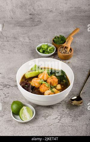 Tom Yam Spicy Thai soup with fish meatball, seafood, coconut milk, mushroom and chili pepper in white bowl on stone background Stock Photo