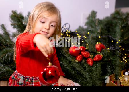 Young girl helping her mother decorating the Christmas tree, holding some Christmas baubles in her hand. Stock Photo