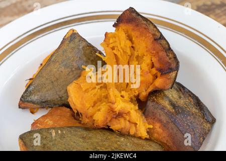 Close up shot of baked pumpkin in a plate with wooden background. Stock Photo