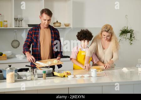 Father frying onion when mother helping son to roll out pasta dough Stock Photo