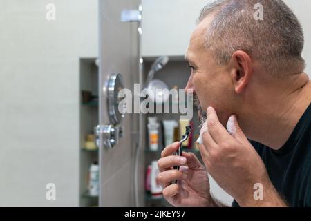 Middle-aged handsome man using razor in bathroom Stock Photo