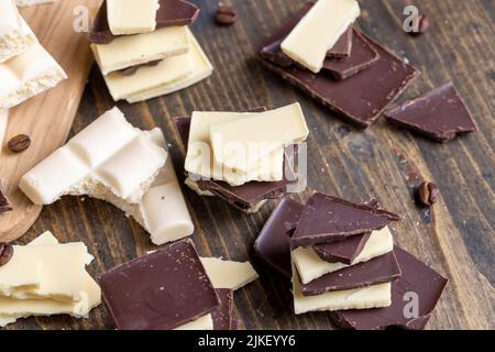 broken into pieces tiles of white and milk and dark chocolate , chocolates broken into pieces and pieces on the table Stock Photo