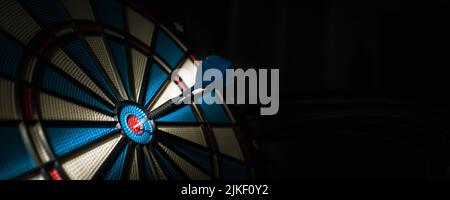 A dart hitting the center of target with copy space in dramatic light and shadow. Bullseye target or a dart dashboard for financial business planning and targeting with winner goal concept Stock Photo