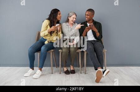 Teeth chattered rhythms. a group of people laughing at a funny visual from a smartphone against a grey wall. Stock Photo