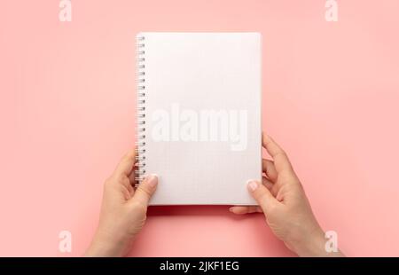 Notepad mockup. female hands holding blank spiral notepad or calendar over pink table background. hands shows open notebook. Female hands holding blan Stock Photo