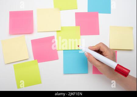 Many colored empty sticker notes on white wall. hand with red marker ready to write. blank Sticker notes on white background. Mockup sticky Note Paper Stock Photo
