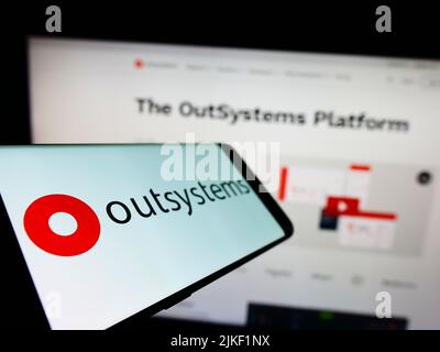 Mobile phone with logo of low-code software company OutSystems on screen in front of business website. Focus on left of phone display. Stock Photo