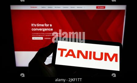 Person holding smartphone with logo of US cybersecurity company Tanium Inc. on screen in front of website. Focus on phone display. Stock Photo