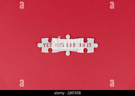 Motivational words - Yes you can do it. Positive motivation text on white puzzle jigsaw on red background. Self confidence and encouragement concept. Stock Photo