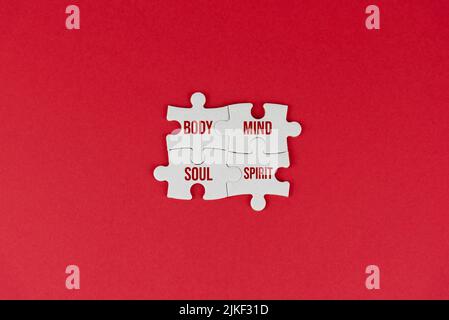 Body mind soul and spirit. Spirituality connection concept with single word on four jigsaw puzzle on red background. Spiritual words for mental health Stock Photo