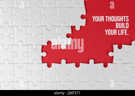 Life inspirational and motivational quote - Your thoughts build your life. With white jigsaw puzzle with some missing pieces on red background. Stock Photo