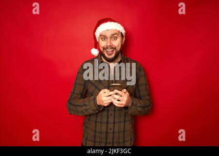 a happy excited man in Santa Claus Christmas hat with phone in his hands rejoices received sensation Stock Photo