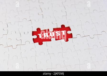 TRUST text on white jigsaw puzzle background with missing piece on red. Business partnership and team work concept. Stock Photo