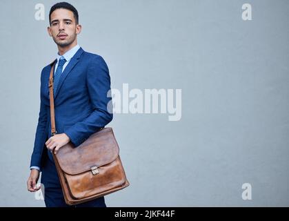 All set for another day in the office. Cropped portrait of a handsome young businessman posing in studio with his satchel against a grey background. Stock Photo