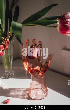 pink glass hand holding dried pink rose, with pink tulips and japanese flowering quince Stock Photo