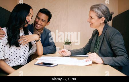 Securing their financial future. an affectionate young couple meeting with their mature female financial advisor. Stock Photo