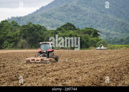 Sugar Cane farm workers on a tractor towing a disc plough tilling the soil on a recently harvested paddock in Redlynch Valley, Cairns, QLD, Australia. Stock Photo