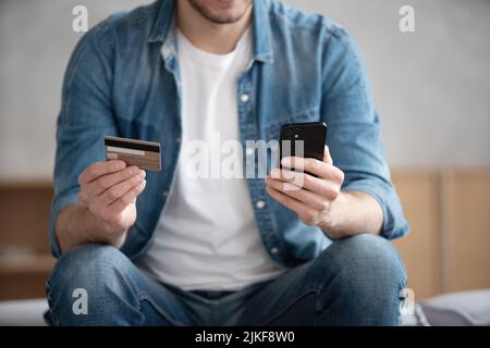 Close up of smiling young Caucasian man hold cellphone make online payment purchase with credit card, happy male shopping online on smartphone, use in Stock Photo