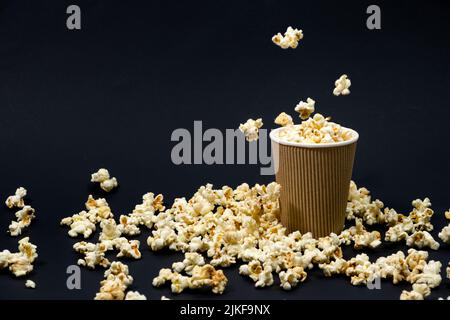 Popcorn is poured into a paper brown glass on a black background with place for text Stock Photo