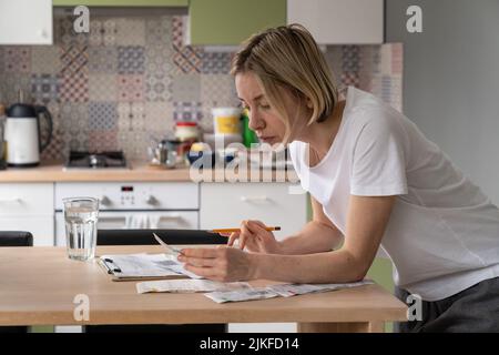 Thoughtful woman of middle age looks at bills and counts sums sitting at table closeup Stock Photo