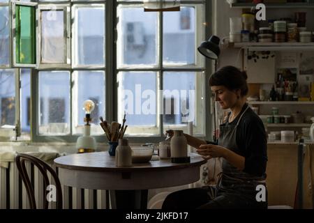 Young skilled lady concentrated on modeling jug from raw clay enjoys hobby creating vase Stock Photo