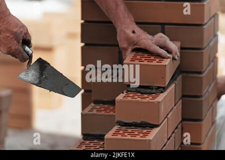 Worker lays brick on cement mortar. Construction of brick fence. Bricklayer at work. Stock Photo