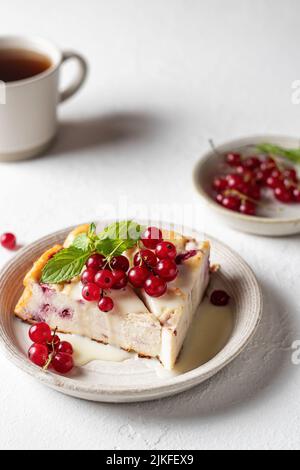 Cottage cheese casserole with fresh summer berries currant on white table with tea cup for healthy breakfast. Vertical orientation Stock Photo