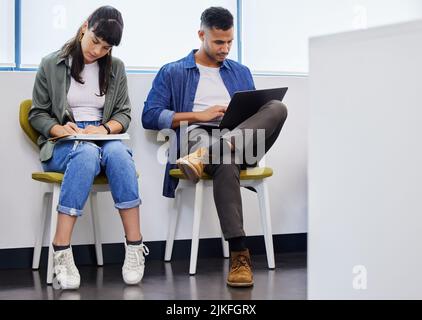 There is a way to do it betterfind it. two young adults using their devices while waiting to be interviewed in a modern office. Stock Photo