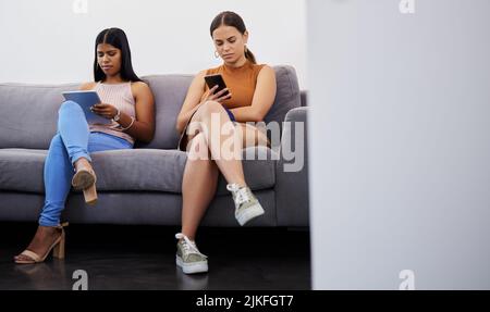 One step closer to our dream career. two young women using their devices while waiting to be interviewed in a modern office. Stock Photo