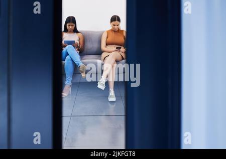 Focused on the goal ahead. two young women using their devices while waiting to be interviewed in a modern office. Stock Photo